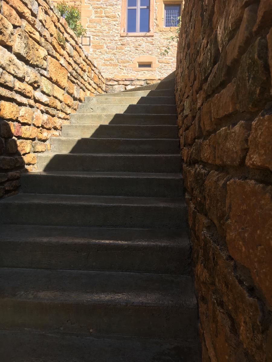 vue dans l'escalier, on voit la maison en pierre dorée en face typique de la région du beaujolais